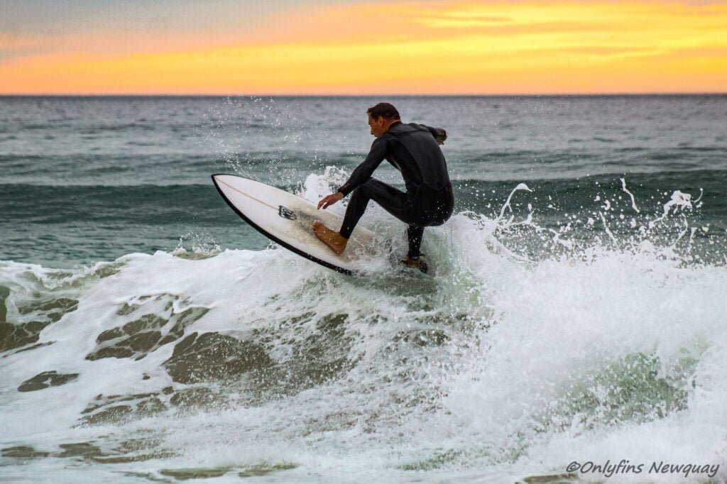 Surfer riding a wave at Perranporth Beach with a stunning sunset in the background